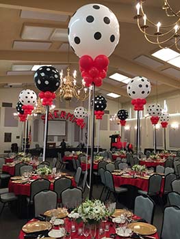 These heilum filled 30 inch polka dot covered black and white centerpiece balloons are each adorned with red collar balloons.  They float 5 feet over each table anchored to a floral arrangement on each table.
