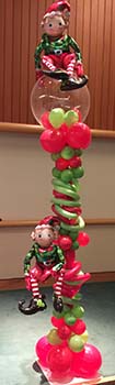 Two mylar balloon elves are joyfully playing on this five foot high freestanding column of clear and spiraling holiday color balloons.