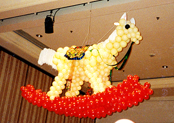 This six foot  balloon rocking horse is suspended from the ceiling of a Fairmont Hotel ball room for a toyland theme holiday party where guests were surrounded by toys as big as themselves