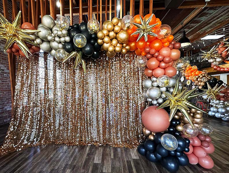 An organic style grland decoration created from fall color latex balloons partially framing a shimmering gold backdrop.