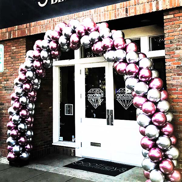 This swirled balloon arch is is created from silver and mauve chrome balloons to provide an customer-catching entrance to this business.