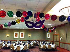 Garlands of 18 inch red, emerald green, gold and blue shiny mylar balloons radiate out from the center of the ceiling to decorate this Mardi Gras-themed event.