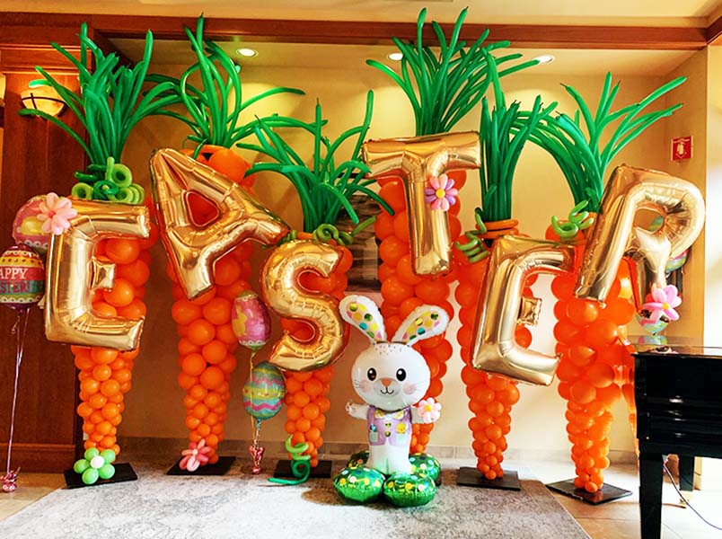 Two easter theme decorations made with mylar and latex balloons on poles placed in the yard of a residence