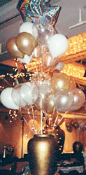 Clusters of gold and white latex balloons topped by a silver mylar star balloon float above an 18 inch tall gold urn to provide an elegant classic table cetnerpiece