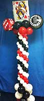 A red, white and black balloon column topped by a giant playing card and dice balloons serves as an area decoration for casino theme events