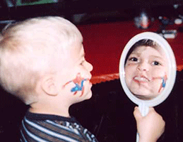 Boy looking in mirror enjoying his Batman face paint tatoo