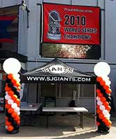 Balloon columns in team colors flanking an information table for a Giants baseball event
