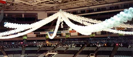 Garlands of white, clear and silver latex balloons spaning the San Jose, Ca. arena in spoke-like pattern to create the perception of a giant tent for guests at a corporate event on the arena floor.